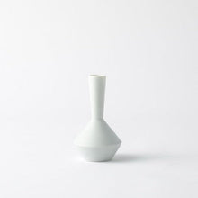 A minimalist, small ceramic vase with a wide, rounded base and a very narrow neck, finished in a glossy off-white glaze, set against a seamless light gray studio background.