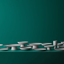 A set of matte white ceramic pedestal dishes and small vessels arranged along the bottom edge of a dark teal-green background.